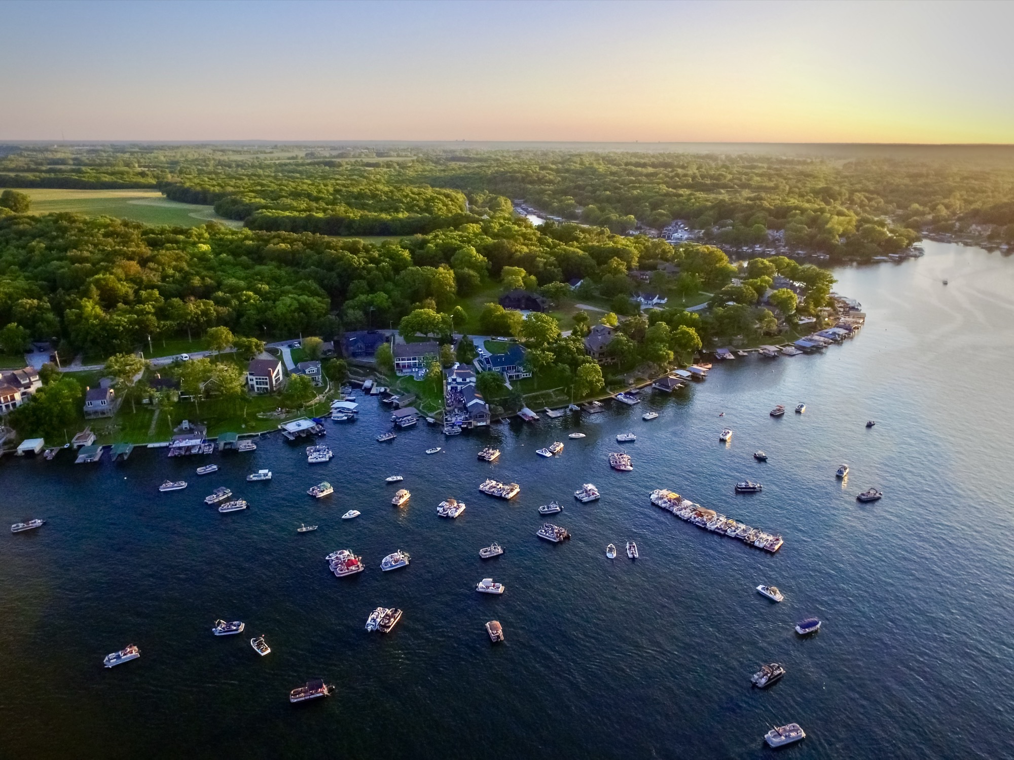 Golden-hour aerial of dozens of boats gathered on Lake Lotawana for a concert