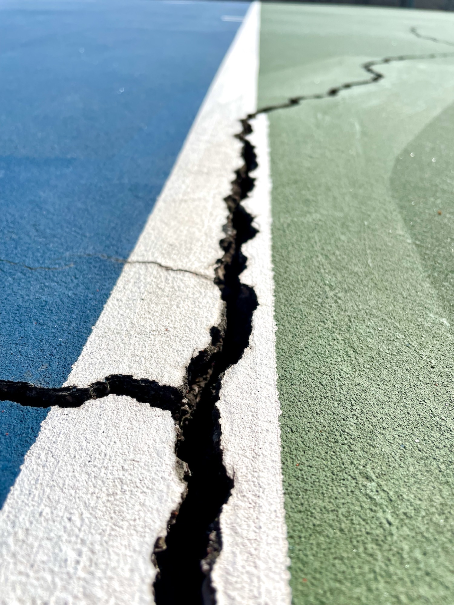 Deep crack running across the surface of the Lake Lotawana tennis courts — built 1975, last resurfaced 2018