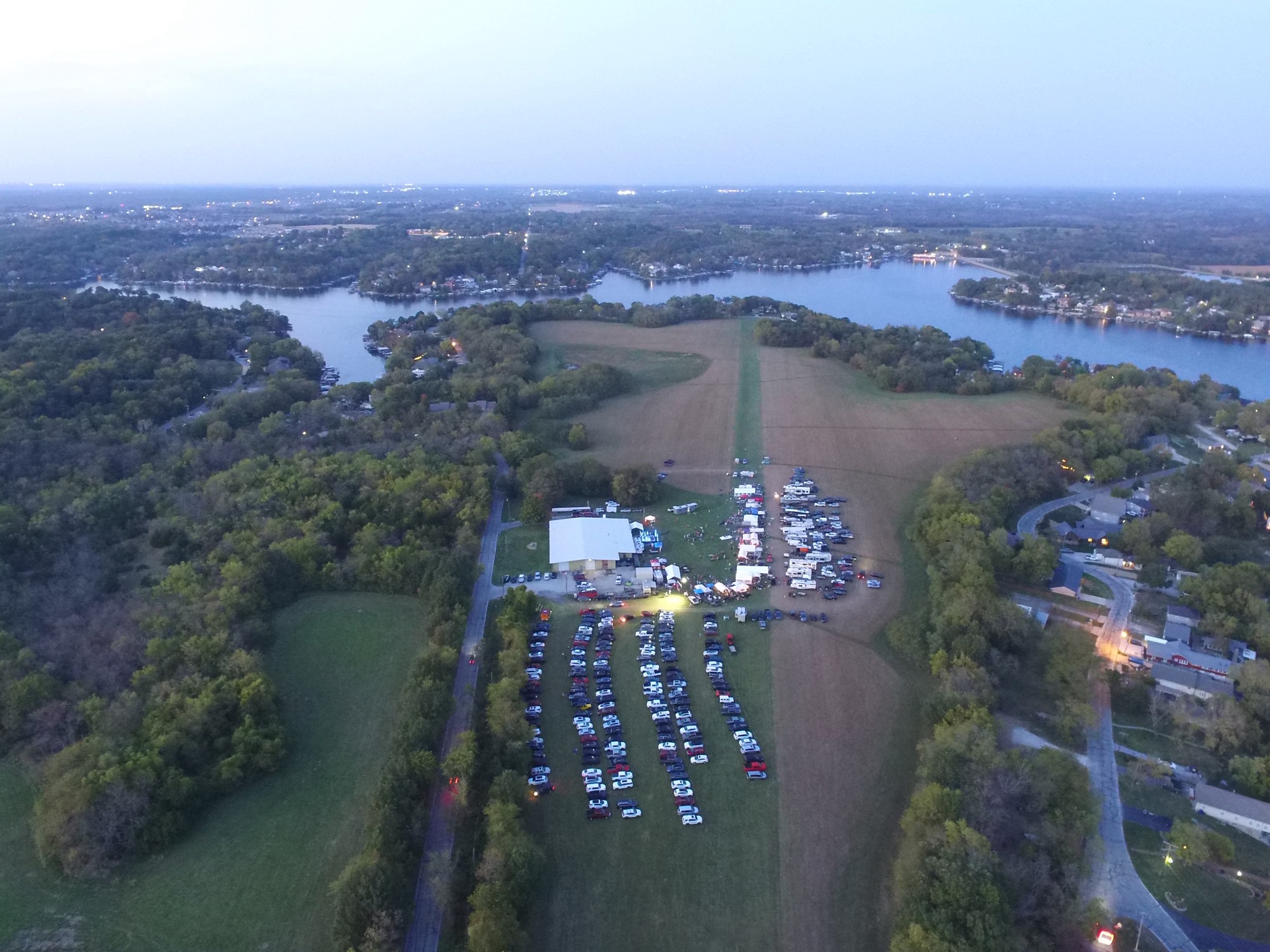 Aerial drone view of Stafford Airfield at dusk during Lotasmoke BBQ competition, with the stage lit up and the lake visible in the background